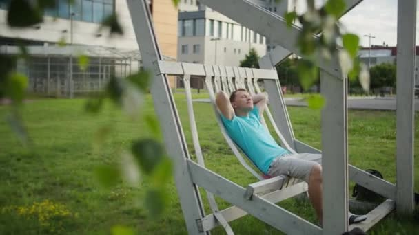 Een jonge man rust op een bank op een zonnige dag, camerabeweging - Video