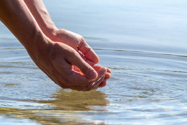 Gros plan des mains coupant l'eau de la rivière avec réflexion. Attraper de l'eau pure dans les mains gouttes tombant dans la surface de l'eau - Photo, image