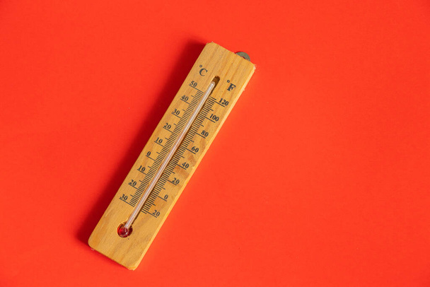 деревянный термометр лежит на красном фоне вблизи
 - Фото, изображение