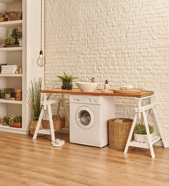 Moderni koti kylpyhuone sisustus pesukoneella ja kirjahylly, puinen pöytä ja pesuallas. - Valokuva, kuva