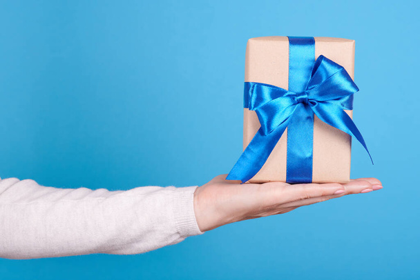 Present box with blue ribbon in hand. - Фото, изображение