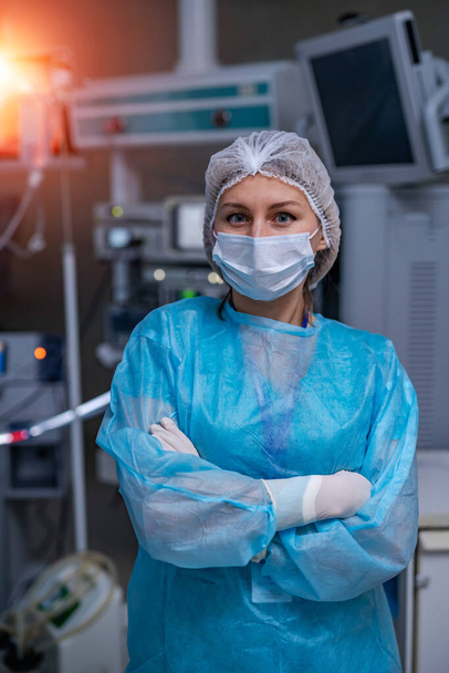 Woman doctor stands cross hands. Blue scrubs. Robotic medical equipment background. - Foto, Imagem