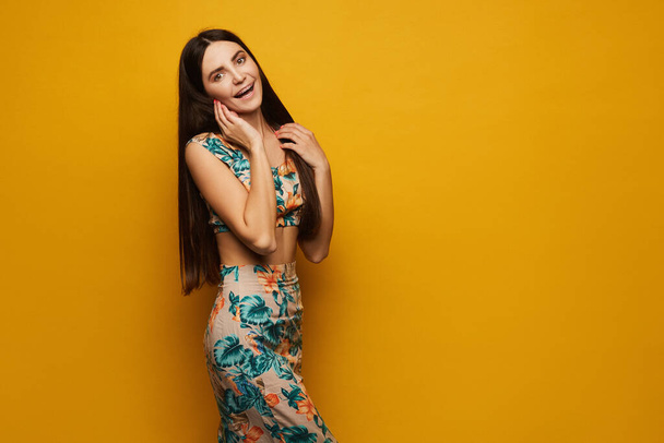 A young Latino woman in top and skirt with flower pattern is posing at the yellow background, isolated with copy space - Фото, зображення