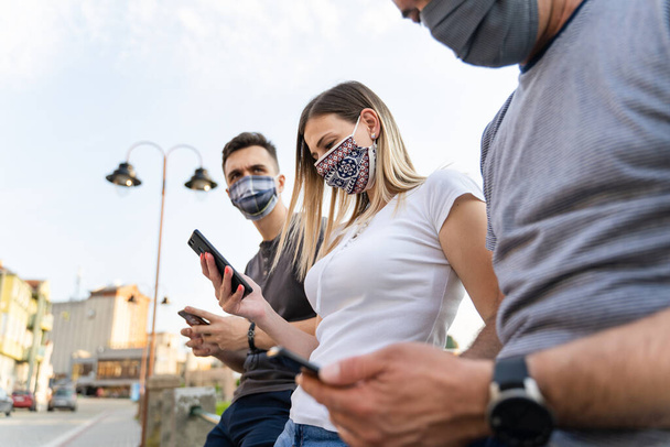 low angle on caucasian man and woman using mobile phone - Modern communication online texting social network messaging - Men and woman with mask hold mobile phones - social distance new normal concept - Photo, Image