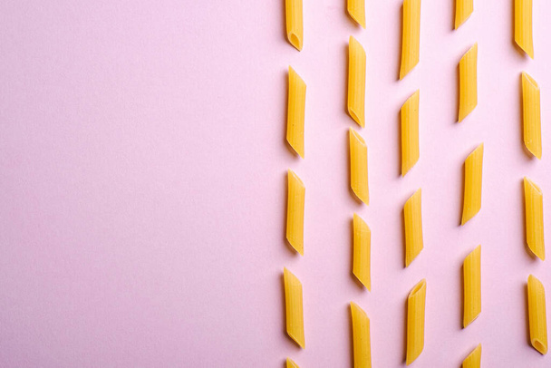 Italian pasta, raw penne tube macaroni pattern on pink background, top view copy space, abstract food - Foto, imagen