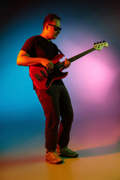 Beyaz tenli genç müzisyen, arka planda neon ışıklarıyla oynuyor. Müzik anlayışı, hobi, festival - Fotoğraf, Görsel