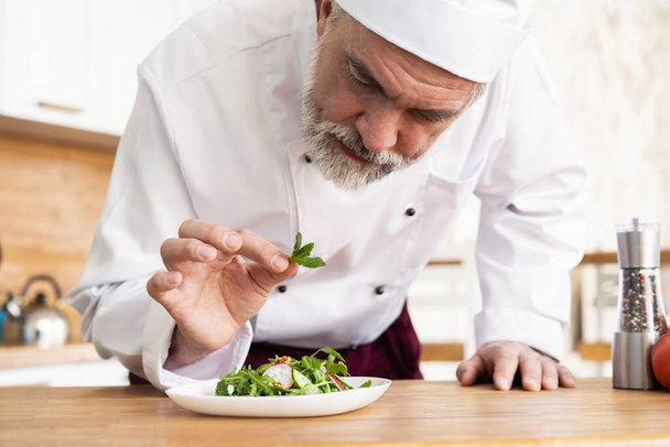 male cook chef decorating garnishing prepared salad dish on the plate in restaurant commercial kitchen. - Zdjęcie, obraz