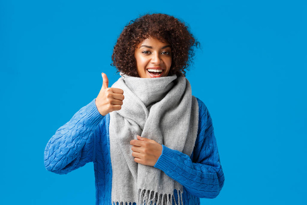 Очень хорошо, да. Симпатичная счастливая африканская женщина в свитере, купила прохладный теплый и удобный шарф, показывающий большой палец в одобрении, порекомендовала магазин, стоящий на голубом фоне
 - Фото, изображение