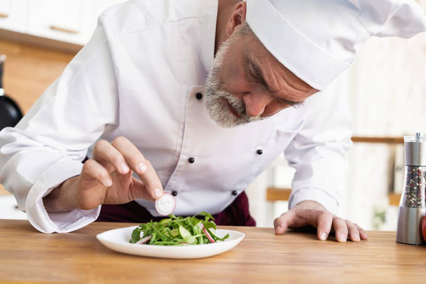 male cook chef decorating garnishing prepared salad dish on the plate in restaurant commercial kitchen. - Photo, Image