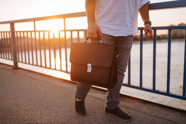 Closeup of black briefcase carried in the hand of a middle-aged businessman on a bridge - Fotografie, Obrázek