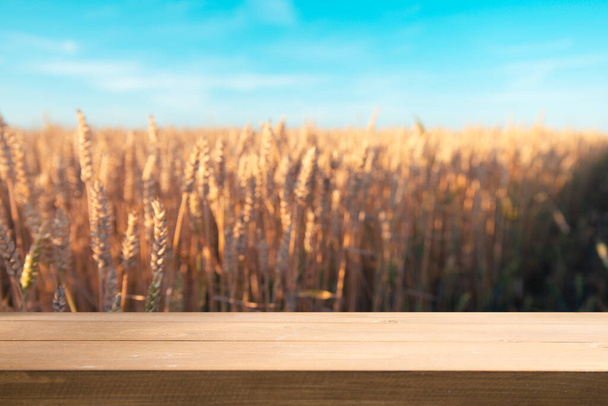 Empty wooden deck table over wheat field with sunset or sunrise. Ready for product montage - Foto, Imagem