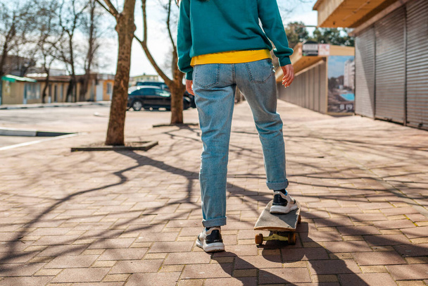 Young beautiful Caucasian woman rides a skateboard.The view from the back. In the background, a street with trees. Close up. Concept of sports lifestyle and street culture. - Photo, Image