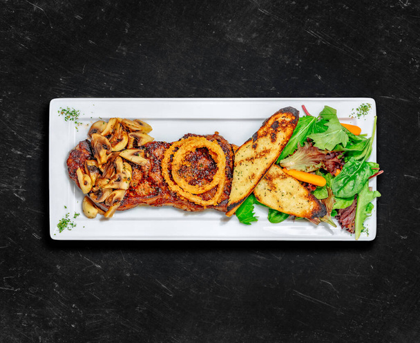 New York Striploin Steak. Healthy food. Grilled steak served with two sides, garlic toast, mushrooms and tossed salad. Chalked background. Top view - Photo, Image