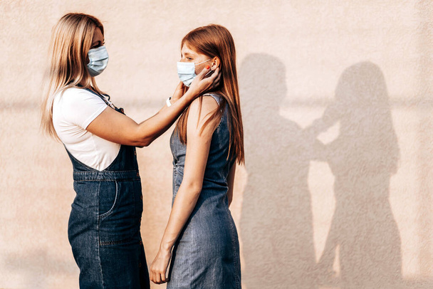 Young mom helping her daughter to put on a medical mask. Corona virus outbreak, protection measures. Copy space - Photo, Image