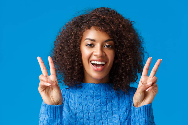 Charismatisch opgewonden en gelukkig, glimlachend vrolijke Afrikaanse Amerikaanse vrouw die positieve vibes, tonen vrede gebaar en grijnzend, genieten van de wintervakantie, nieuwjaarsfeest, zeg kaas - Foto, afbeelding