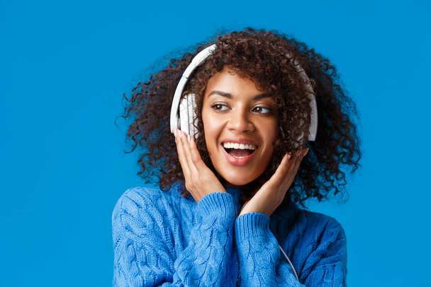Közelkép portré pimasz és gondtalan boldog mosolygós afro-amerikai modern gen-z lány afro frizura, göndör haj, zenét hallgatni fülhallgató mosolygós örömmel, élvezze az új fülhallgató - Fotó, kép