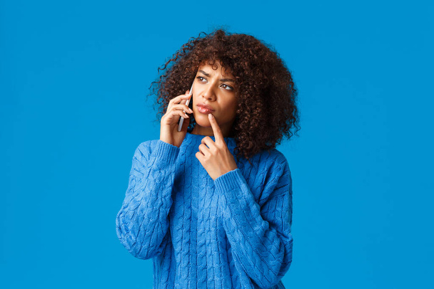 Hmm wait sec let me think. Unsure and pensive african-american attractive woman calling delivery, choosing what food order, touch lip thoughtful, thinking as talking on phone, holding smartphone - Photo, Image