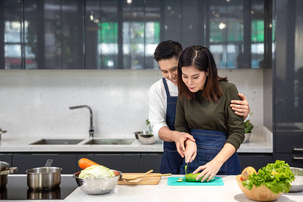 Casais jovens estão ajudando a cortar legumes na cozinha. Asiático casal cozinhar juntos na cozinha
. - Foto, Imagem