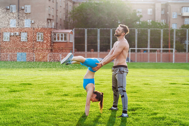 Komik fotoğraf. Spor eğitiminde eğlenen iki sevimli sporcu. Kız baş aşağı duruyor ve erkek ona yardım ediyor, kalçasını tutuyor.. - Fotoğraf, Görsel