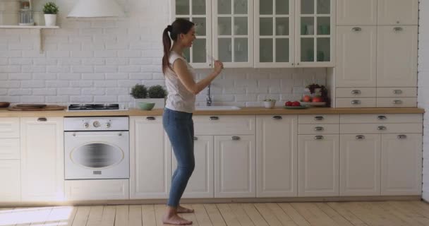 Divertida chica feliz bailando sosteniendo micrófono batidor cantando en la cocina
 - Imágenes, Vídeo