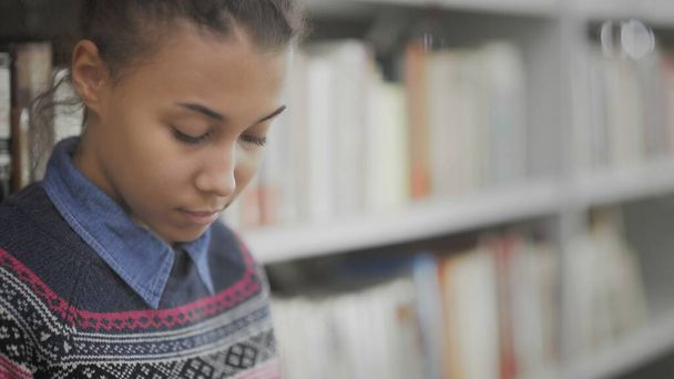 Młoda Afroamerykanka czyta książkę na podłodze w bibliotece uniwersyteckiej. - Zdjęcie, obraz