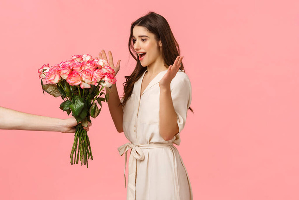 愛、バレンタインデーとロマンスの概念。ゴージャスな白人若いブルネット,ガールフレンドは秘密の称賛者から花を受け取ります,花束のバラを保持配達人に驚いて反応,ピンクの背景 - 写真・画像