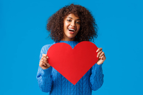Lovely and cute african-american pretty woman with afro haircut, holding valentines day card, big heart and smiling, express love and affection, showing true feelings, search soulmate - Foto, Imagen