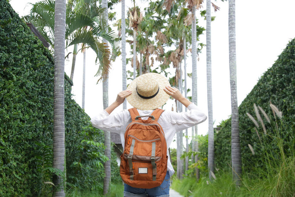 Zadní pohled na turistické ženy nosí slaměný klobouk a oranžový batoh na její letní dovolenou. - Fotografie, Obrázek