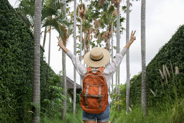 Yaz tatilinde hasır şapka ve turuncu sırt çantası takan turist kadının arkası.. - Fotoğraf, Görsel