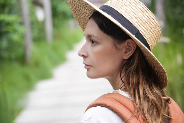 Head shot of tourist woman wearing straw hat and orange backpack on her summer vacation. Close up outdoor portrait of caucasian woman. - Photo, Image