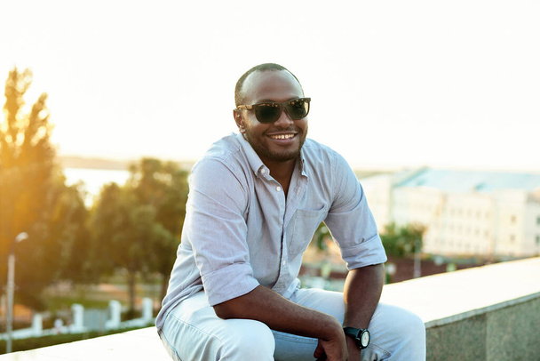 Portret van een lachende vrolijke zwarte man op een zonnige dag tegen de achtergrond van de stad. - Foto, afbeelding