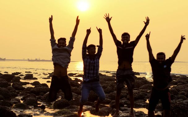 Un grupo de cuatro jóvenes saltando actividad durante el atardecer en la playa del mar
 . - Foto, Imagen