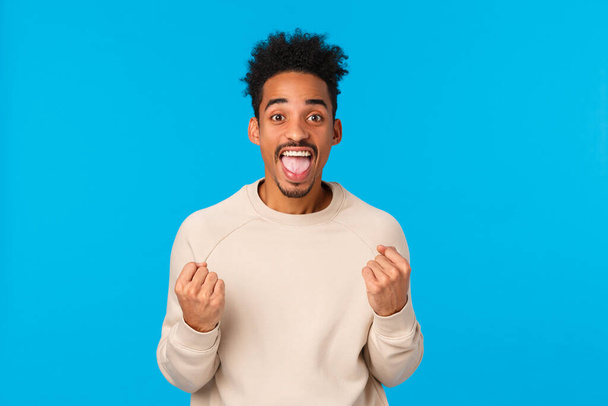 Happy guy got huge chance, winning lottery, got employed awesome company. Attractive african-american male celebrting excellent news, triumphing, shaking fists and smiling joyfully, blue background - Foto, Imagen