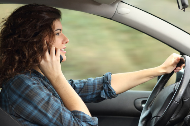 Side view of a woman driving a car and talking on the phone - Foto, afbeelding