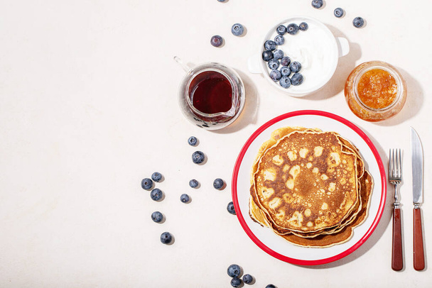 A stack of plain pancakes served with honey and blueberry over a white background. - Фото, зображення