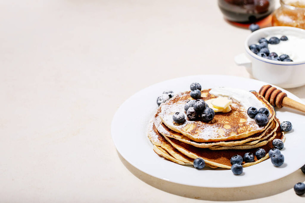 A stack of plain pancakes served with honey and blueberry over a white background. - Φωτογραφία, εικόνα