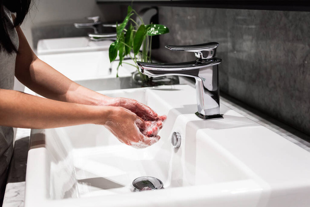 Junge asiatische Frauen waschen sich die Hand mit Seife im Wasserhahn. Neue normale Coronavirus-Prävention. - Foto, Bild