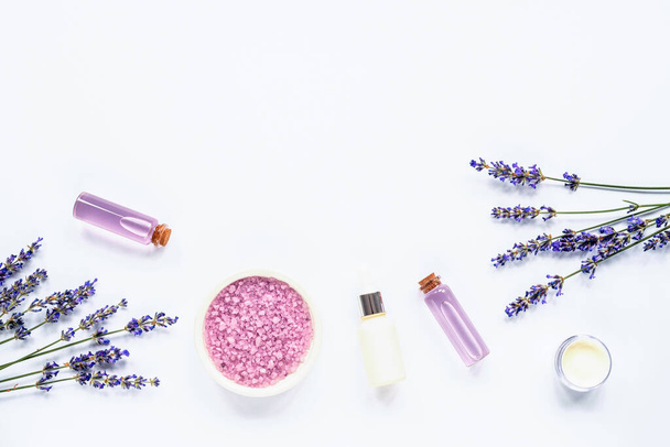 Lavendelbloesem, zeezout, roompot, serum en etherische oliën op witte achtergrond, bovenaanzicht, plat gelegd. - Foto, afbeelding