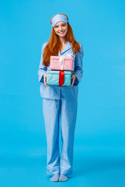 Cheerful and lovely young happy redhead woman waking up early christmas eve congratulating with winter holidays, wearing pyjama and sleep mask, holding boxes with gifts, giving presents - Fotografie, Obrázek