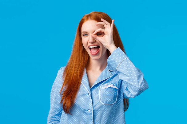 Carefree and sassy happy redhead woman with blue eyes, showing okay, no worries and satisfaction gesture over eye, look through fingers pleased, showing tongue, promote feminine hygiene products - Photo, Image