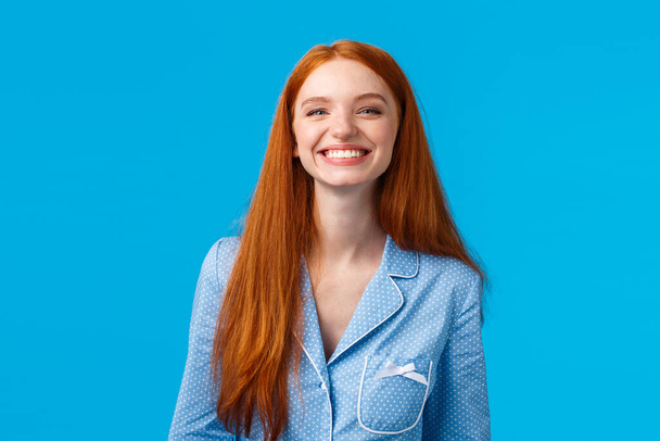 Cheerful girl enjoys life, feelings happy and upbeat, looking mirror at night as finish hygiene procedures, brushed teeth smiling joyfully toothy, standing nightwear over blue background - Photo, Image