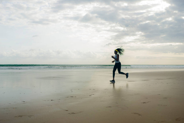 Silhouette of African American woman running on the beach - young attractive and athletic black girl training outdoors doing jogging workout at the sea in fitness and healthy lifestyle - Foto, Imagen