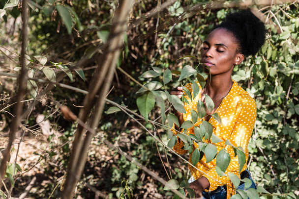 portré gyönyörű fiatal fekete nő sárga ing figyeli a természet egy parkban, koncepció a természet, a társadalmi távolság és portré - Fotó, kép