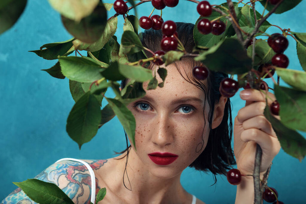 Moda modelo feminino está olhando através de ramo de cereja com fundo azul. Close-up retrato de jovem mulher bonita com sardas
 - Foto, Imagem