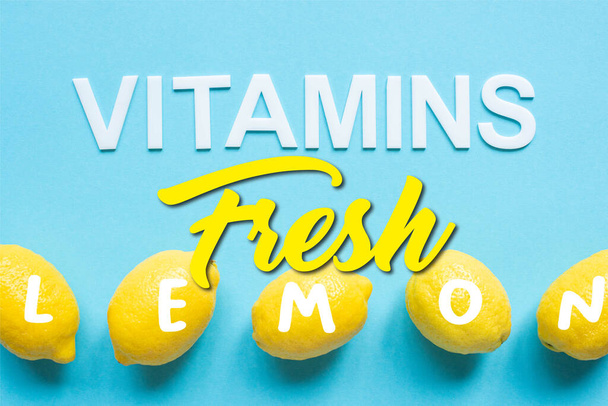 top view of ripe yellow lemons and word vitamins on blue background, fresh illustration - Foto, Imagen