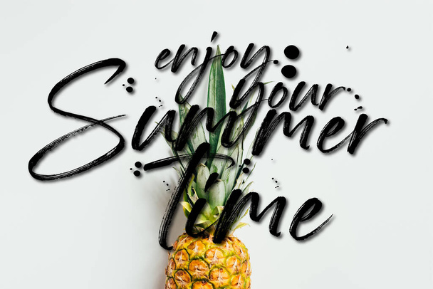 top view of ripe pineapple with green leaves on white background with enjoy your summertime illustration - Foto, immagini