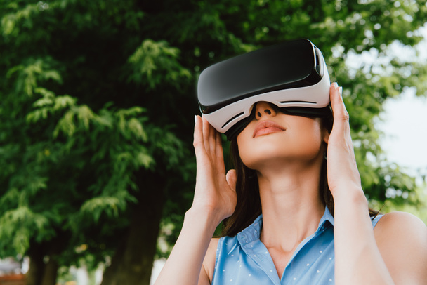 laag gezichtspunt van jonge vrouw aanraken van virtual reality headset buiten  - Foto, afbeelding