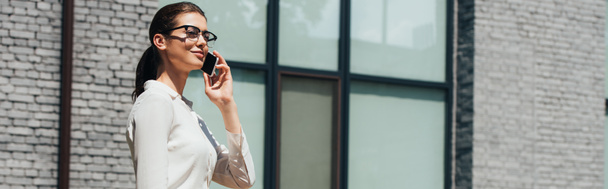 horizontal concept of attractive businesswoman in glasses talking on smartphone and standing near bicycle  - Foto, imagen