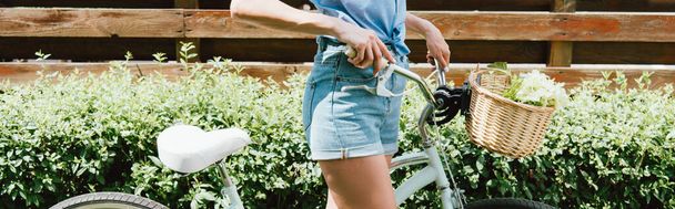 panoramic crop of young woman standing with bicycle near fence - Φωτογραφία, εικόνα