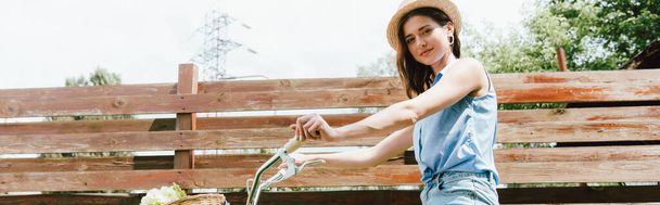 website header of happy girl in straw hat looking at camera near fence and bike - Foto, Imagem